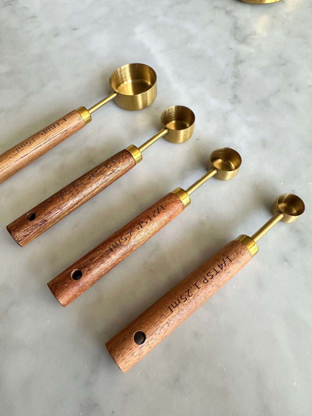 Wood-handled gold measuring spoons with holes at the handle ends