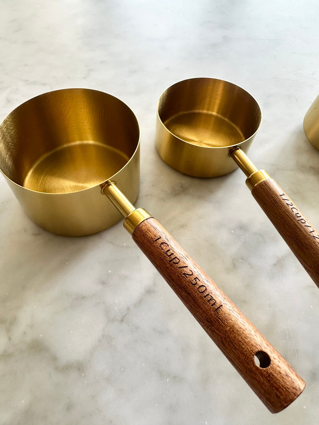Two gold measuring cups showing the bowl shape and wooden handles