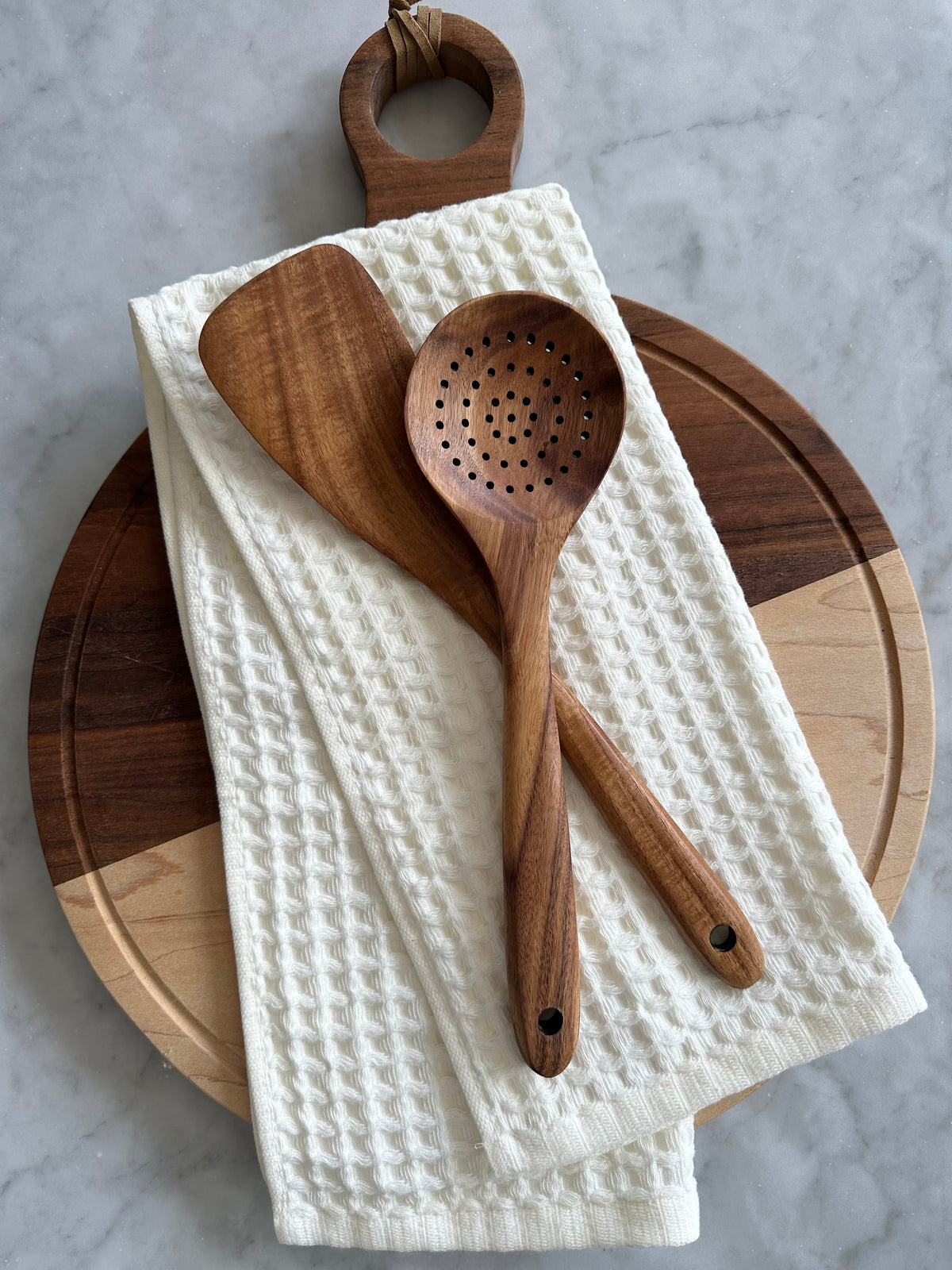 Teak wood spatula and perforated spoon on a towel and cutting board