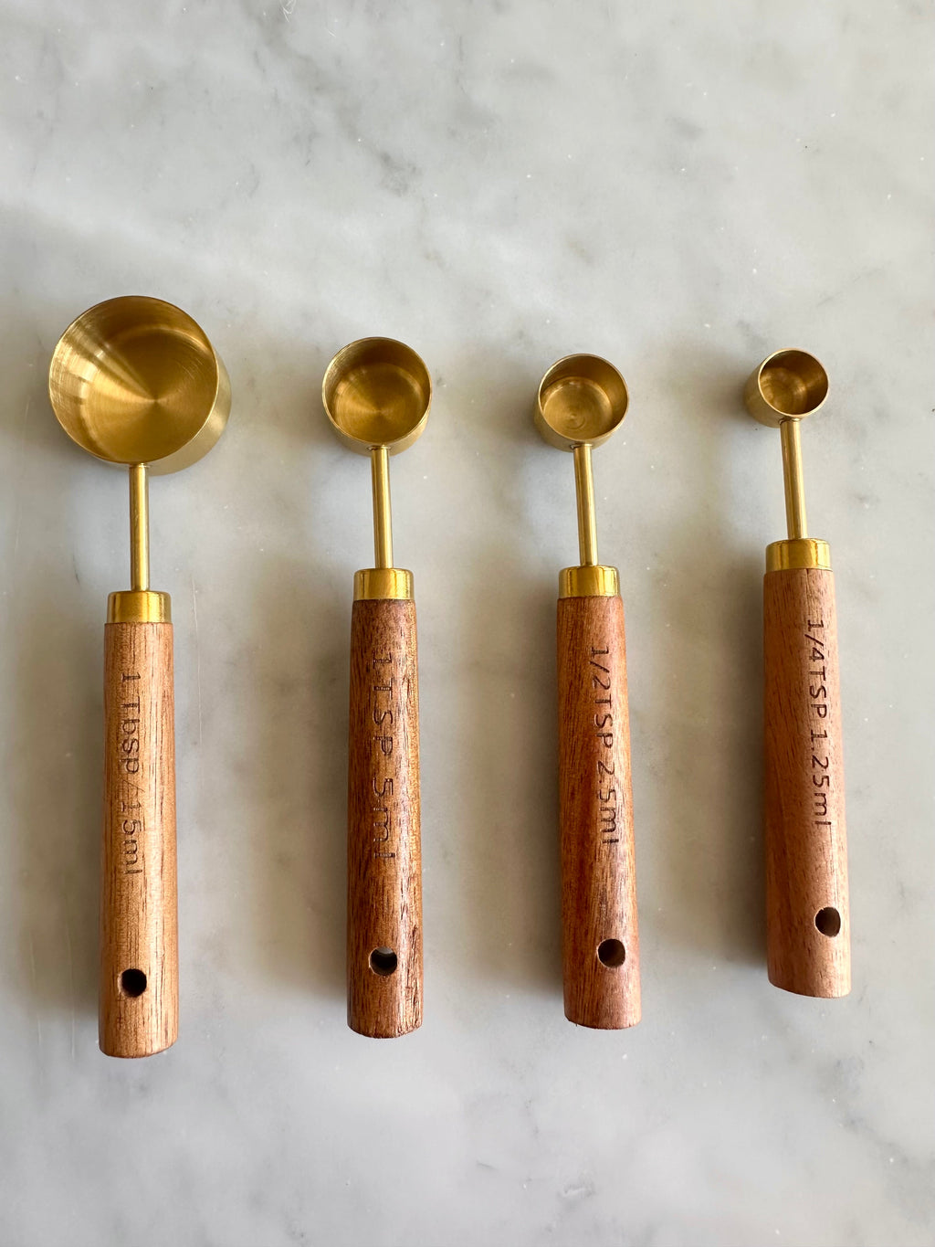 Four wood-handled gold measuring spoons showing tablespoon and teaspoon markings