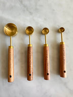 Four wood-handled gold measuring spoons showing tablespoon and teaspoon markings