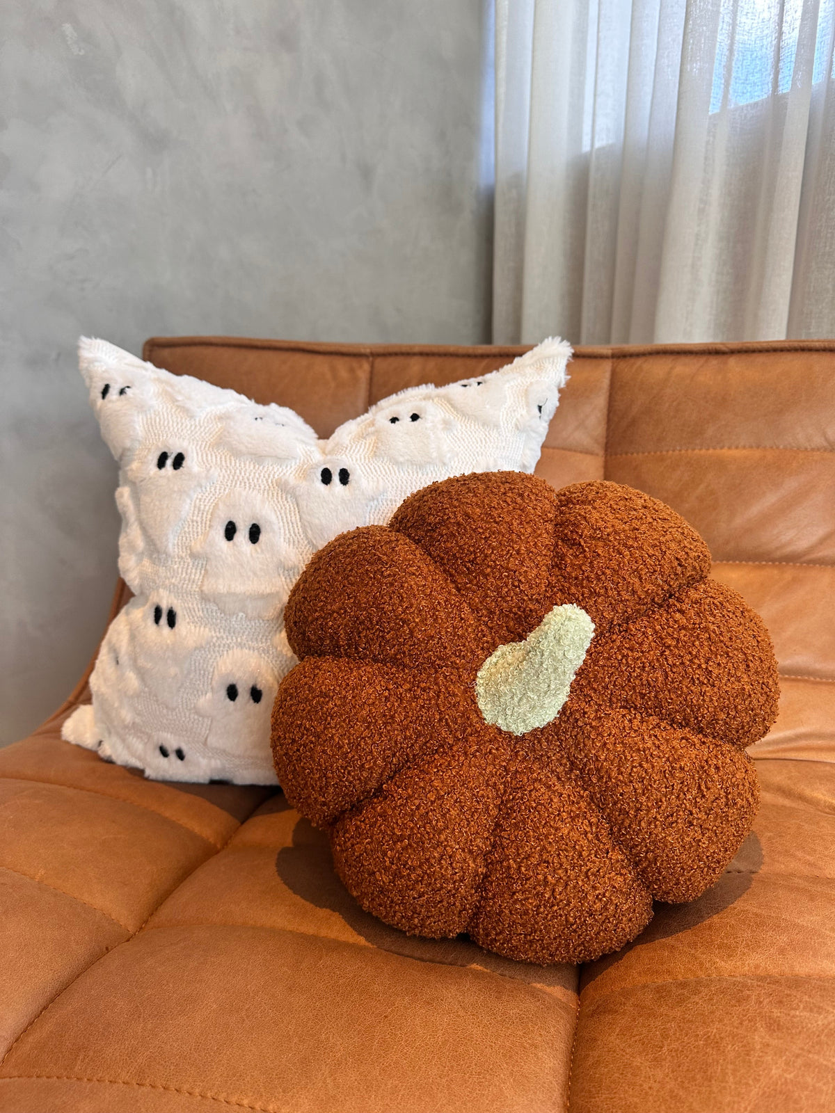 Orange pumpkin pillow with a pale green stem on a leather couch