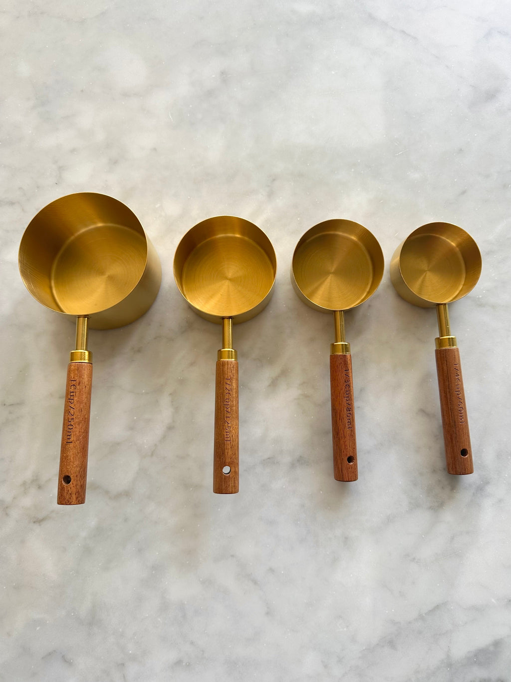 Four gold measuring cups with acacia wood handles and marked capacities