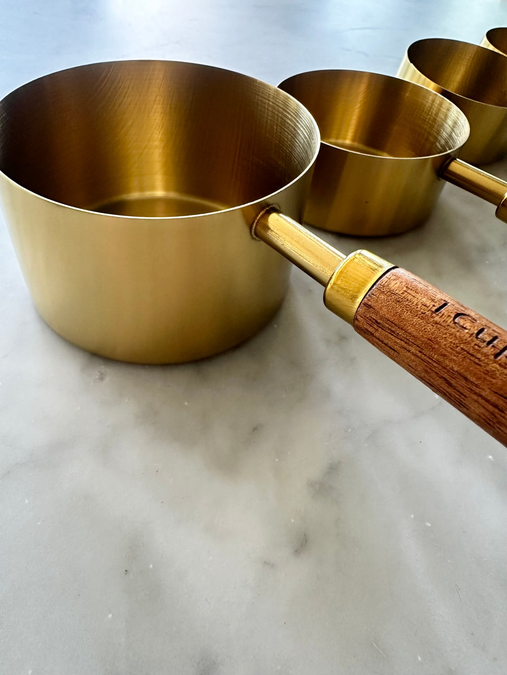 Close-up of three gold measuring cups with wooden handles