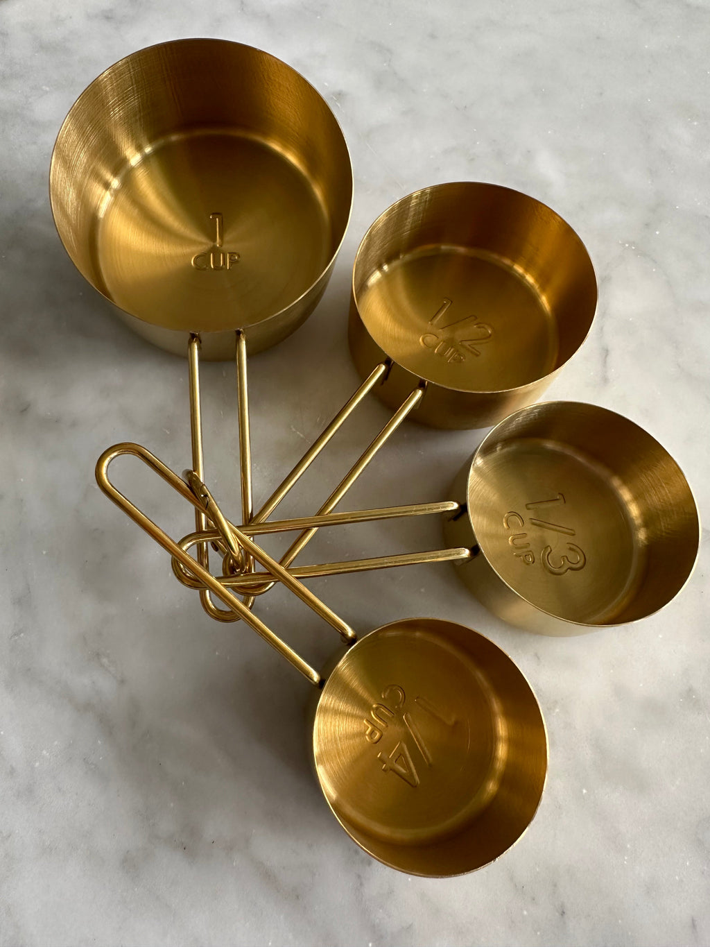 Four gold measuring cups with size markings inside the bowls