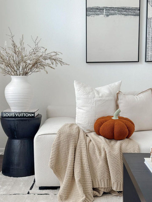 Orange pumpkin pillow on a white couch beside a cream throw