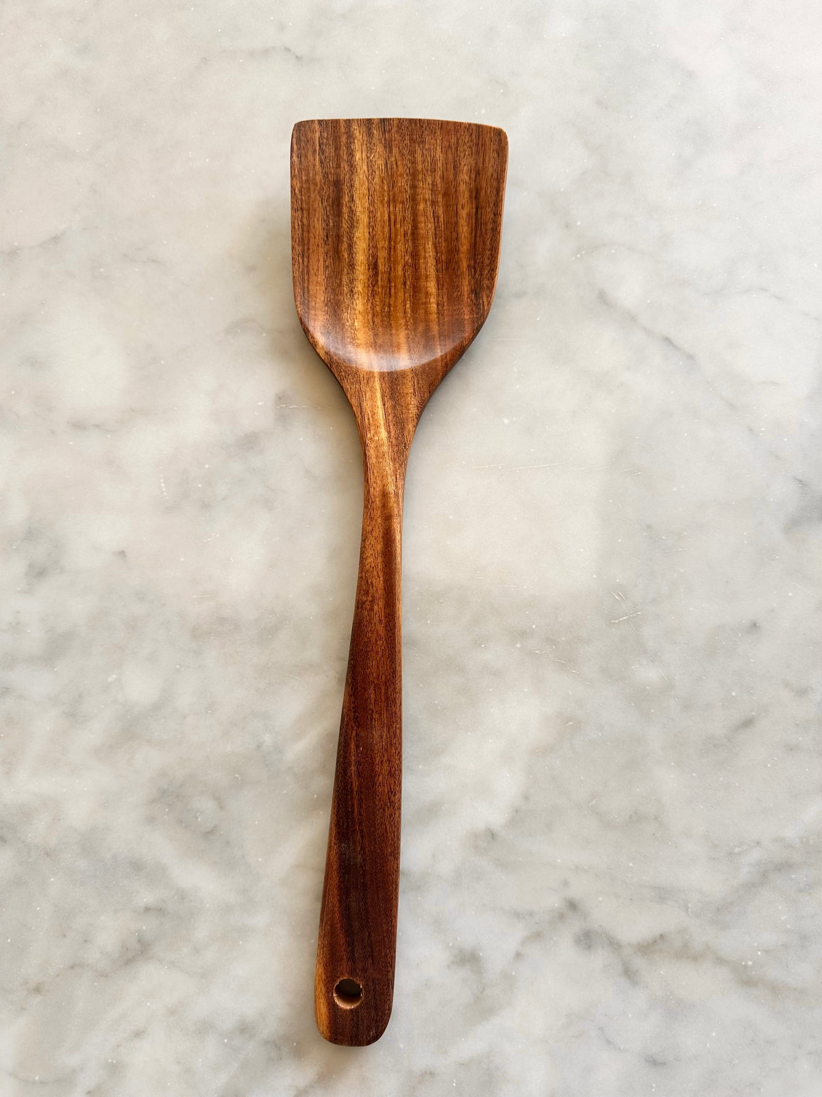Front view of a broad teak wood spatula with a hanging hole