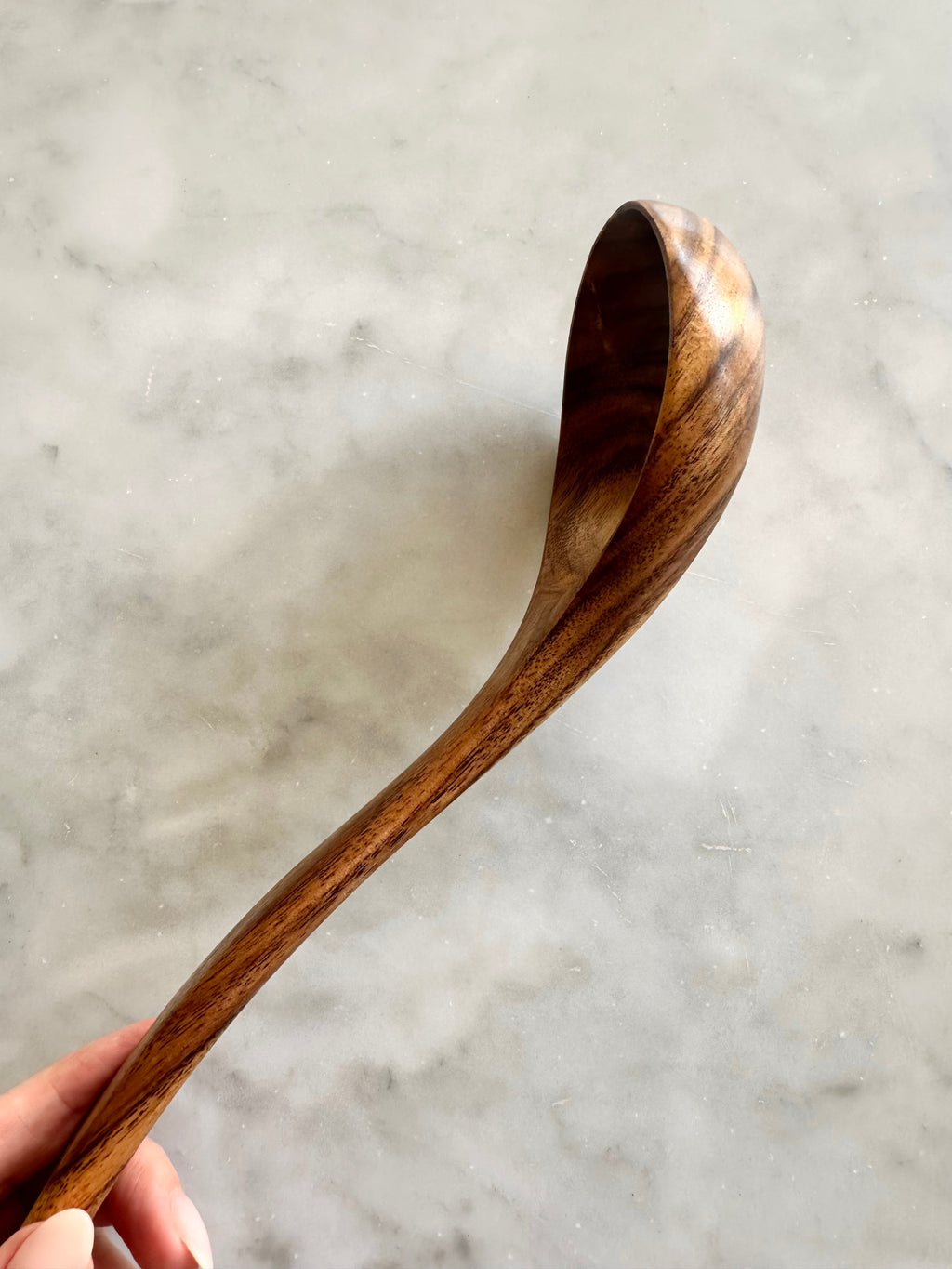 Side view of a teak wood ladle showing its curved bowl