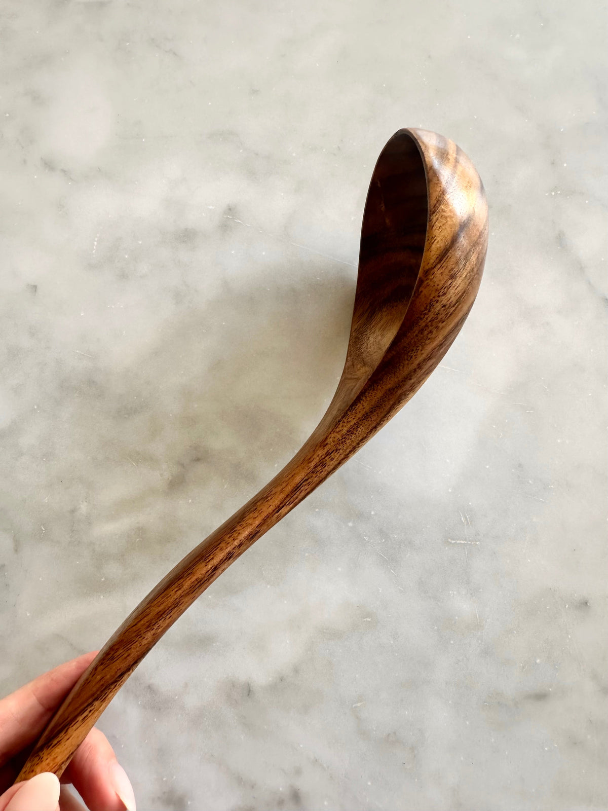 Side view of a teak wood ladle showing its curved bowl