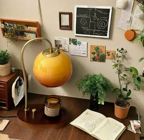 Orange candle melting lamp with a curved stand beside an open book and plants