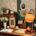 Orange candle warmer lamp above a jar candle on a table beside books and flowers