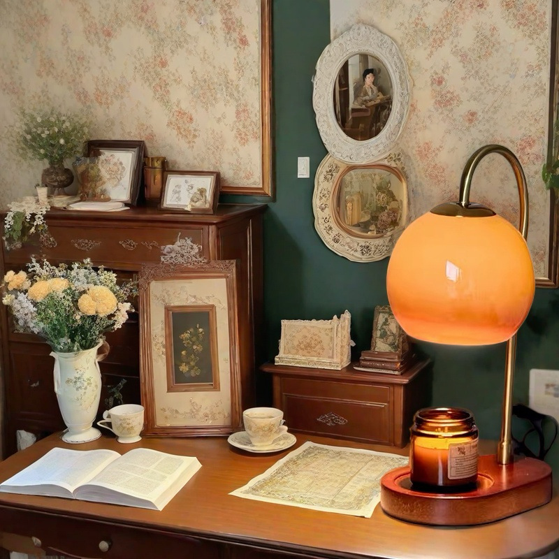 Orange candle warmer lamp above a jar candle on a table beside books and flowers