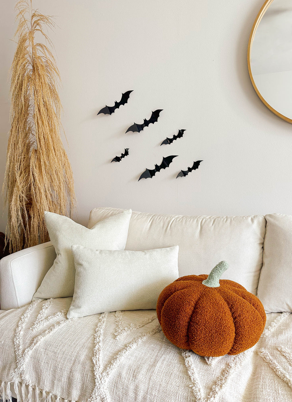 Orange pumpkin pillow on a white sofa beneath bat-shaped wall decorations