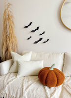 Orange pumpkin pillow on a white sofa beneath bat-shaped wall decorations