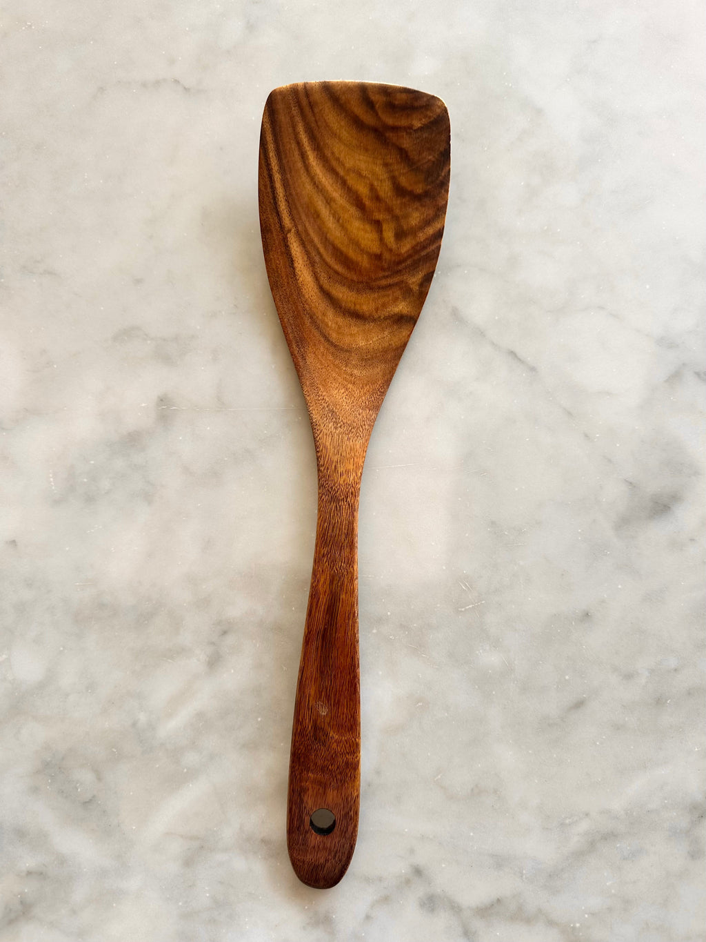Front view of a narrow teak wood utensil with a flat working end