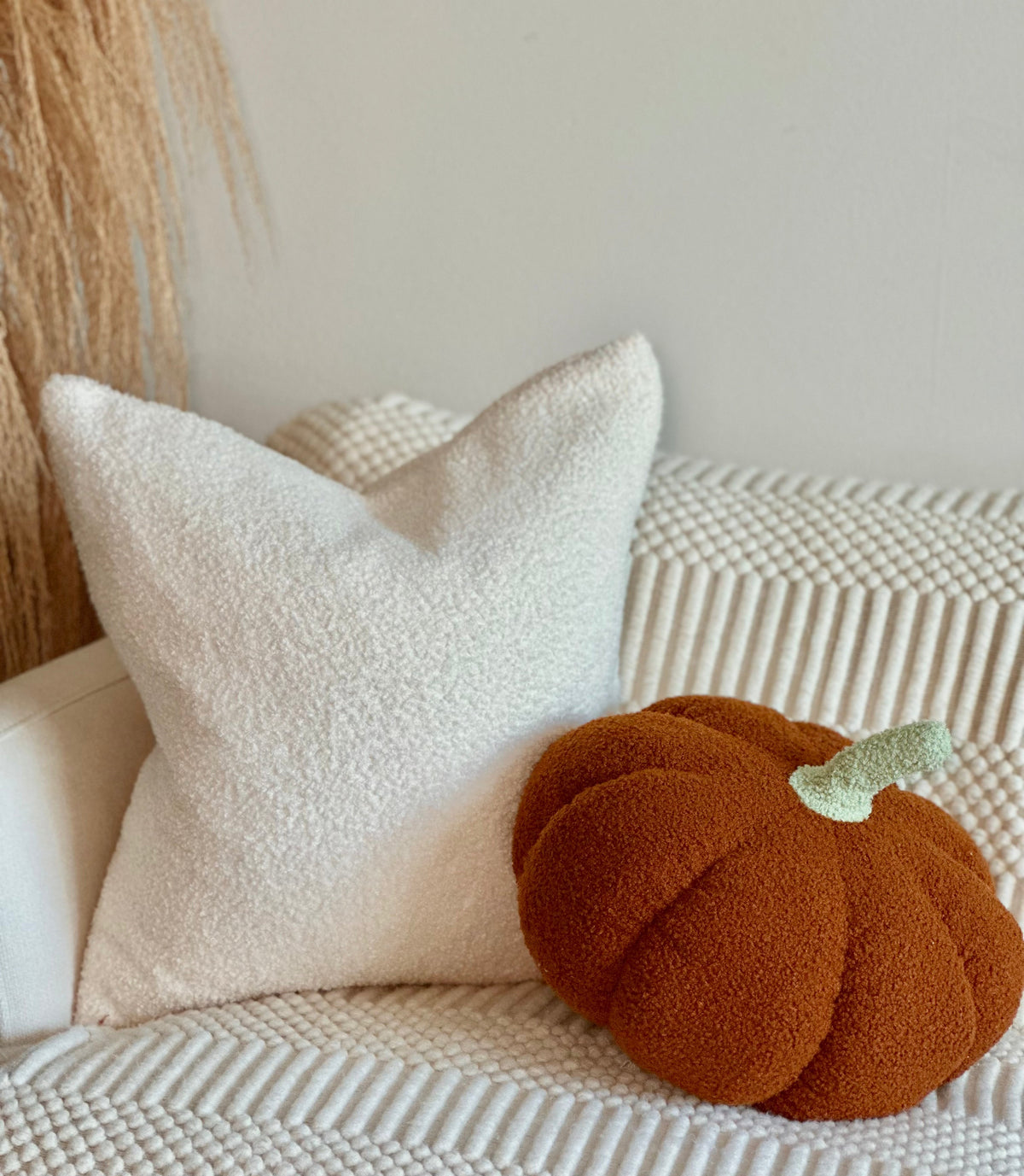Orange pumpkin pillow with a pale green stem among cream cushions