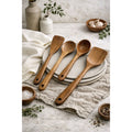 Four teak wood kitchen utensils arranged on plates beside a towel
