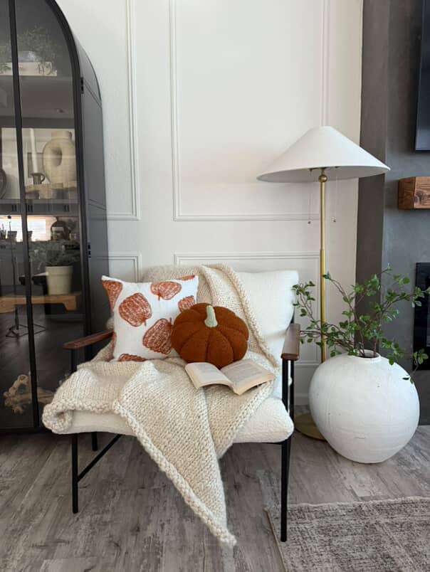 Orange pumpkin pillow styled on an accent chair with a throw blanket