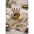 Eight gold measuring cups and spoons with wooden handles arranged beside a towel