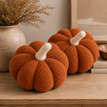 Two burnt orange sherpa pumpkin pillows with light-colored stems on a table