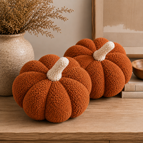 Two burnt orange sherpa pumpkin pillows with light-colored stems on a table