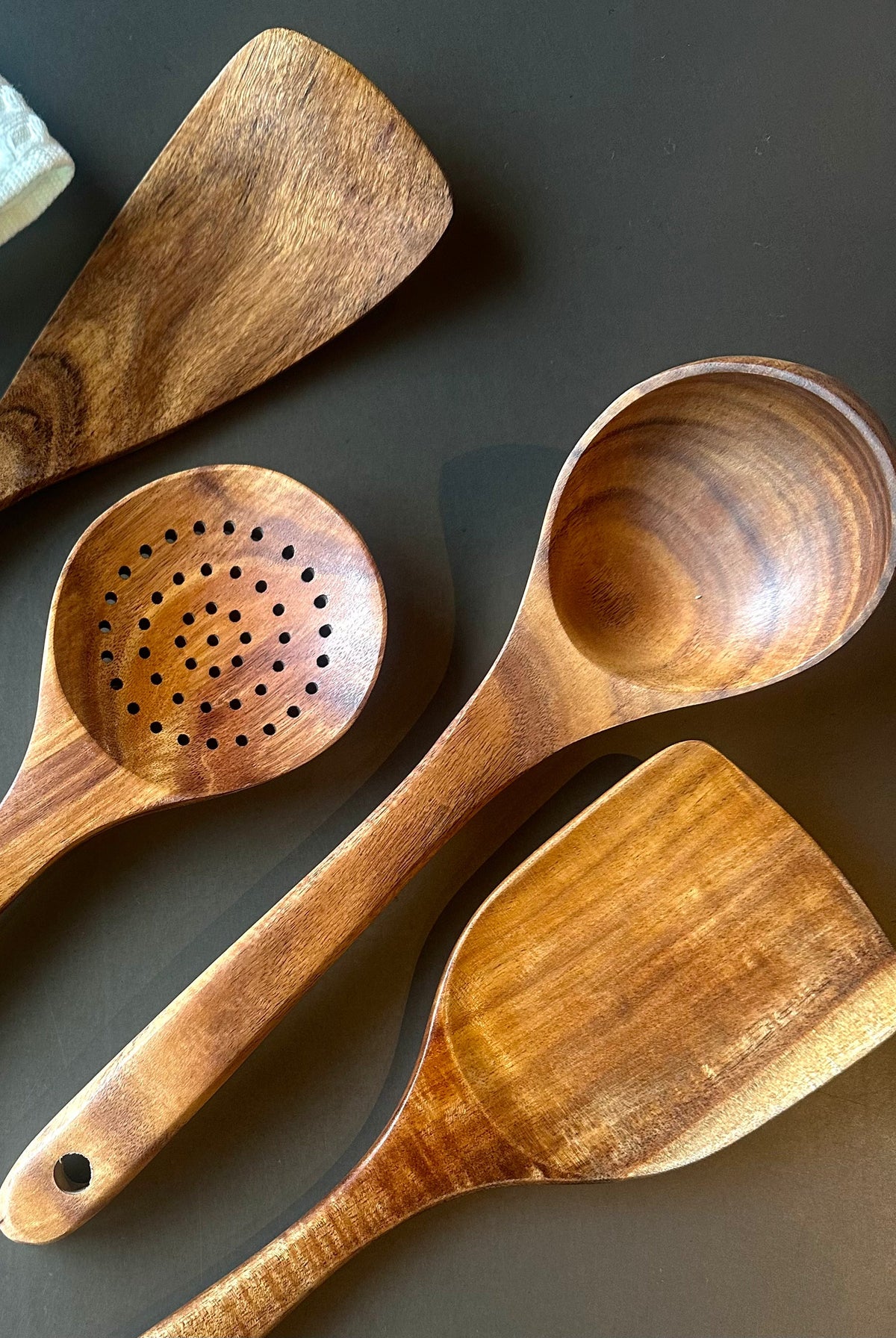 Close-up of teak utensils showing a perforated spoon, ladle, and spatulas