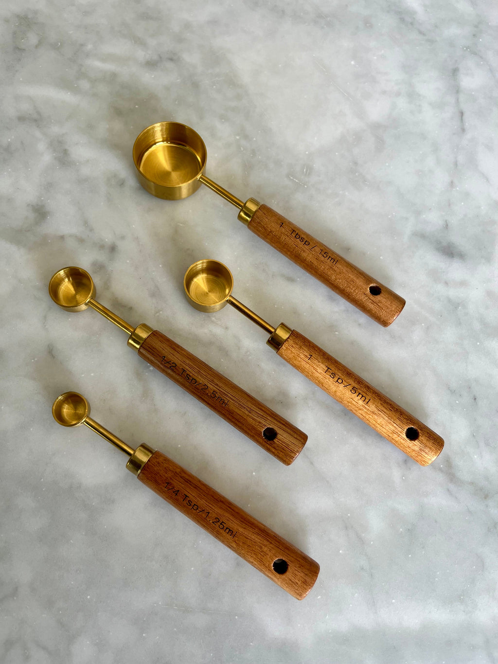 Four gold measuring spoons with wooden handles arranged diagonally
