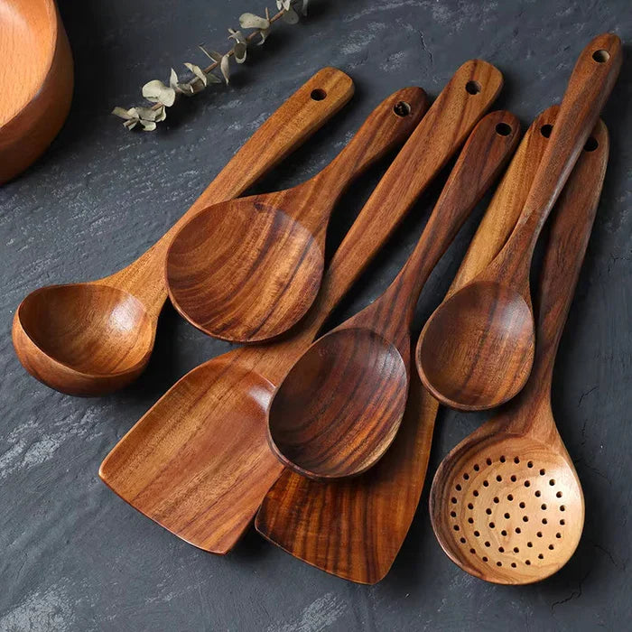Seven teak wood cooking utensils arranged on a dark counter