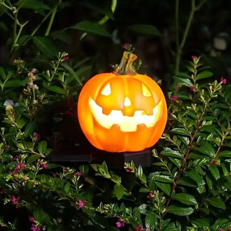 Single illuminated pumpkin stake light beside green shrubs