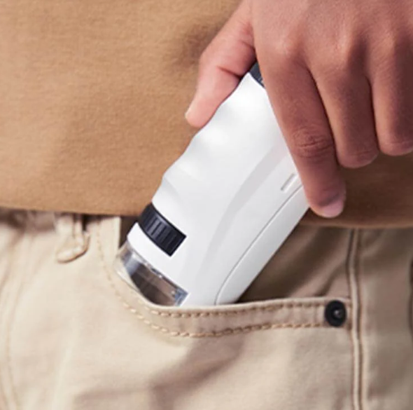 White pocket microscope being placed into a clothing pocket
