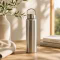 Stainless steel water bottle with a carry-loop lid on a table beside books