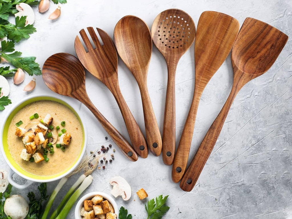 Six teak wood cooking utensils arranged beside a bowl of food