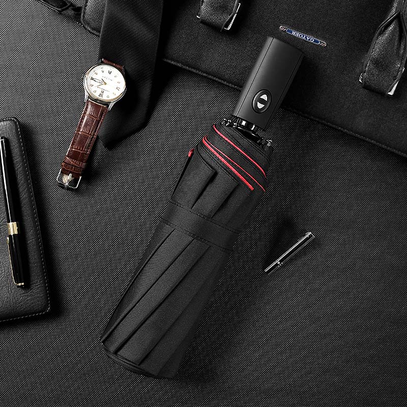 Folded black umbrella with red trim beside everyday accessories