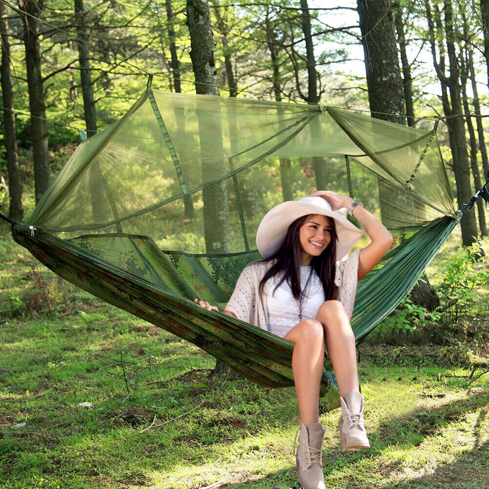 Green camping hammock with raised mesh net set up between trees
